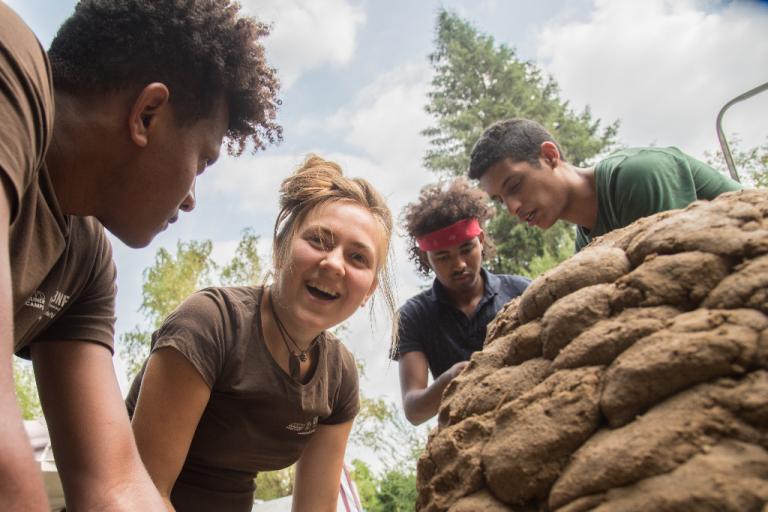 Vier Teilehmende lachen, während sie neben ihrem Lehmbackofen stehen. | Foto: Hendrik Silbermann (ARTWORKs)