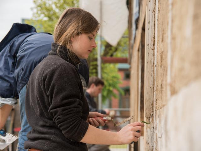 In Feinarbeit werden die Fugen verputzt | Foto: Hendrik Silbermann (ARTWORKs) Teilnehmerin verschließt Fugen an der Fassade mit Lehm