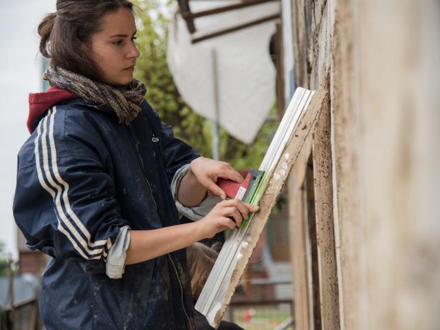 Die Oberfläche der Lehmwand wird glatt gezogen | Foto: Hendrik Silbermann (ARTWORKs) Teilnehmerin zieht den Lehmputz in einem neuen Gefach glatt