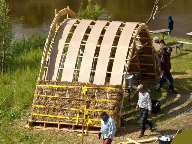 Die Strohballen sehen von außen weich aus, haben aber einen harten Kern. Deshalb müssen sie bei jeder Strohballenbauweise verdichtet werden. Die ersten vier Lagen werden mit LKW-Gurten verdichtet. | Foto: Hendrik Silbermann (ARTWORKs) Die ersten vier Lagen der Strohballen werden mit LKW-Gurten verdichtet.